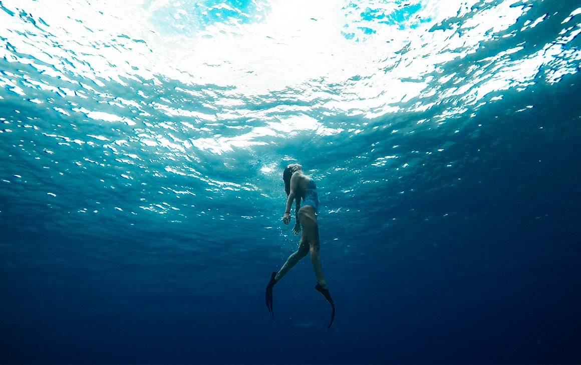 a woman swims towards the surface of the ocean.