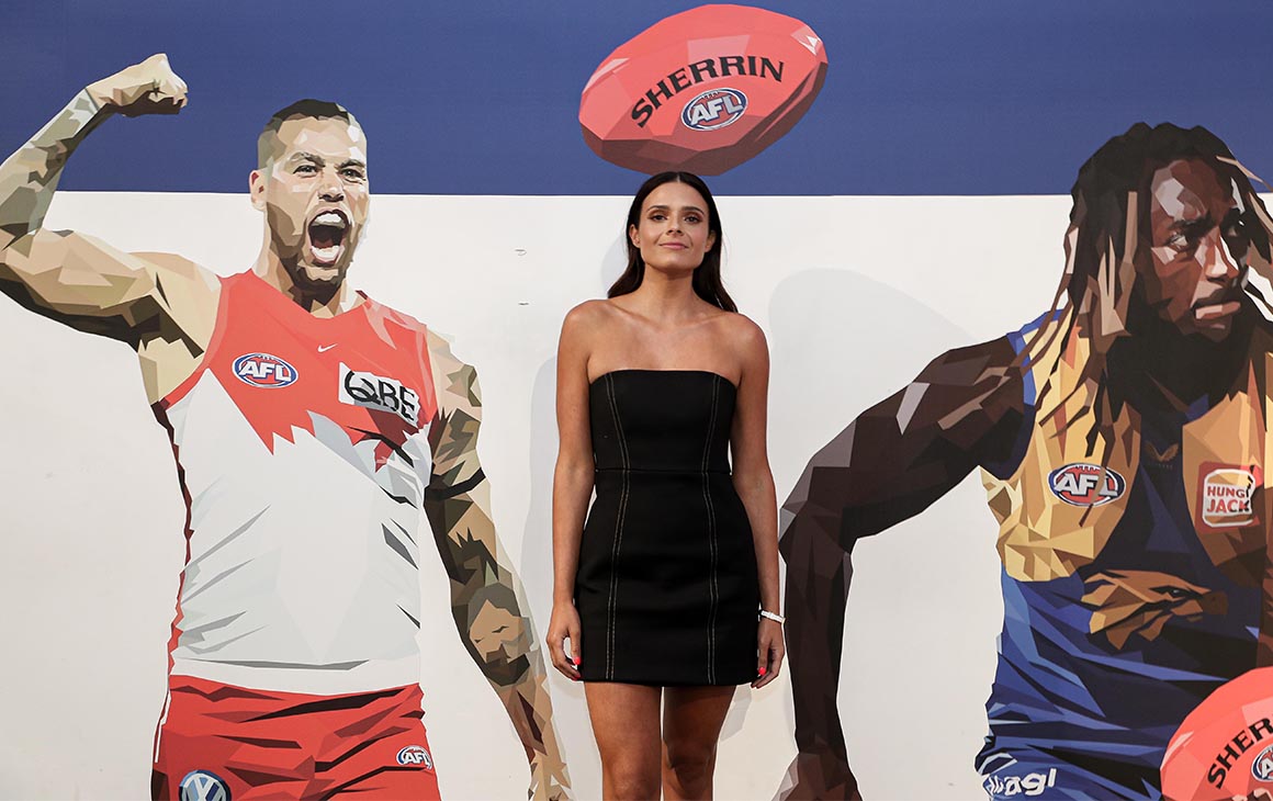 Dom Gauci poses in front of a wall featuring her AFL art work