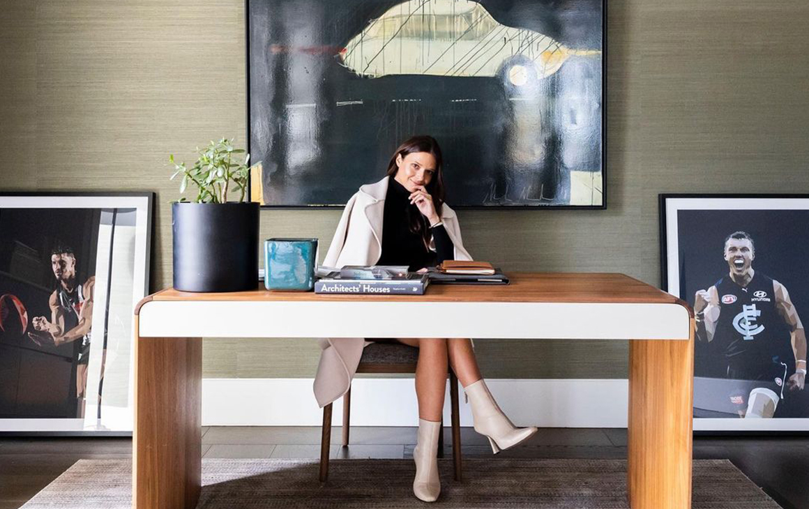 Dom Gauci sits behind a desk, flanked by her art work