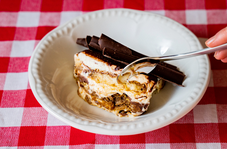 hand with spoon scooping into creamy tiramisu