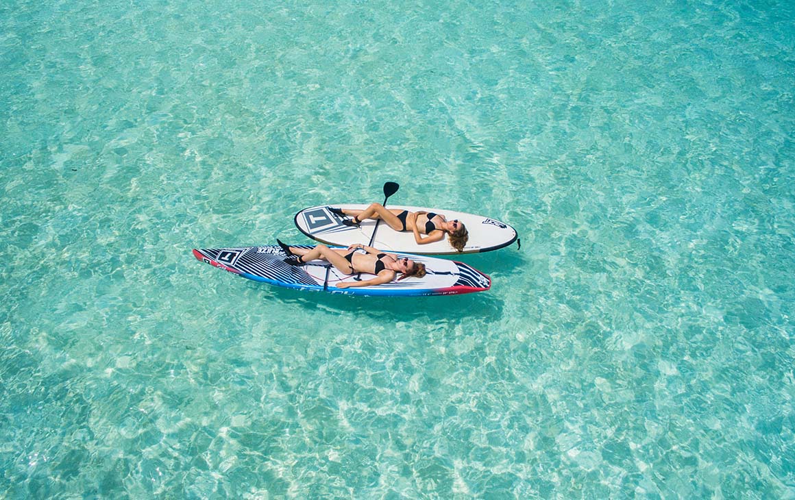 two woman lay on kayaks in crystal clear water