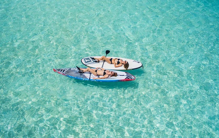 two woman lay on kayaks in crystal clear water