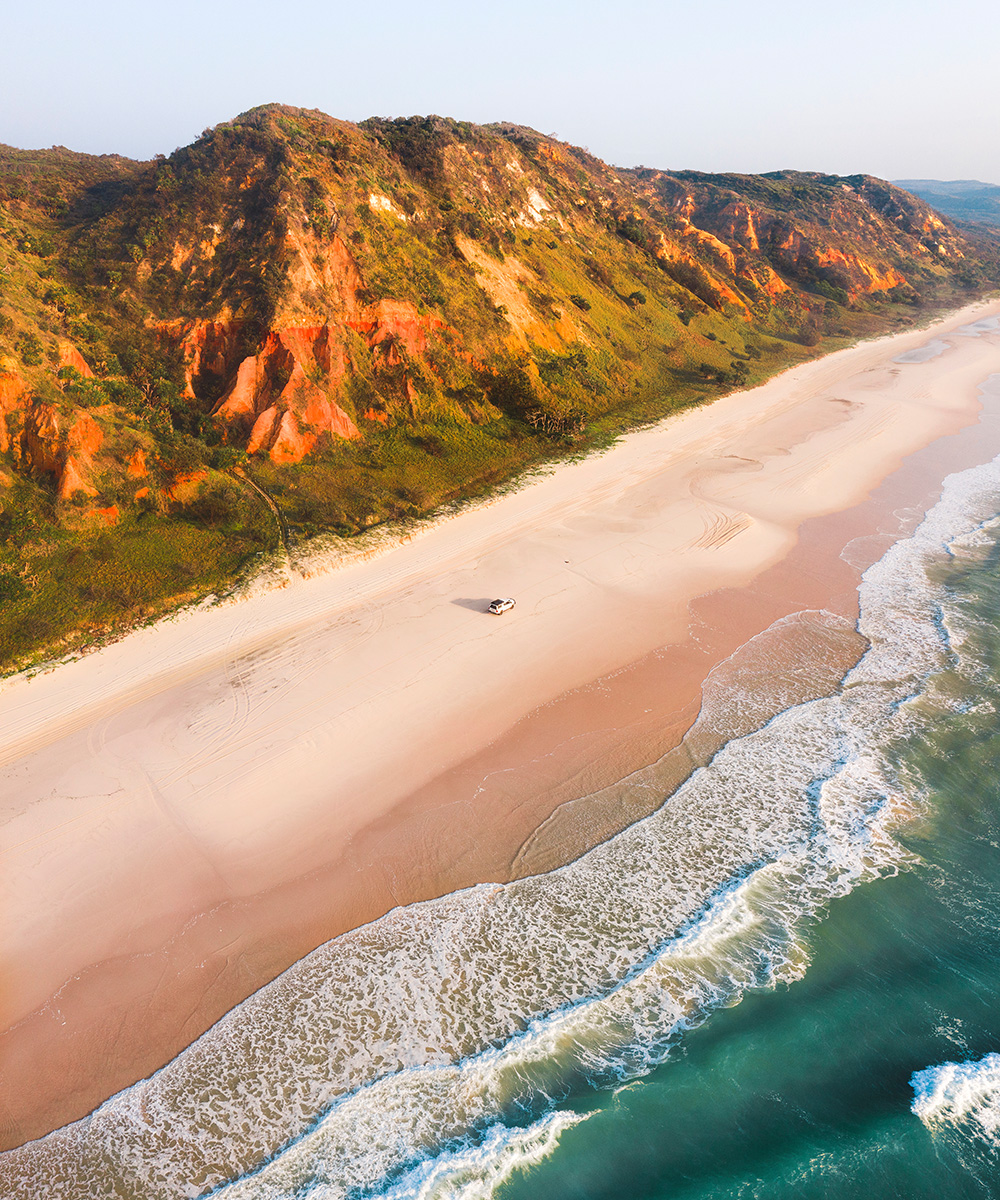 Fraser Island shows off its golden sand beach, blue ocean and the towers rock face behind it.