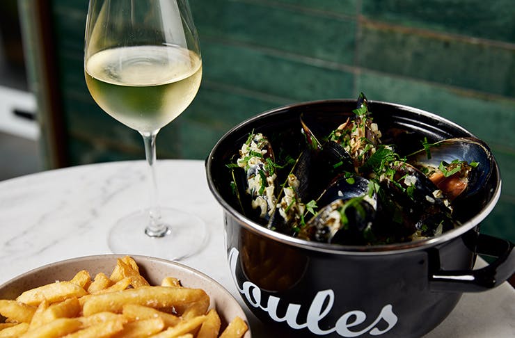 bowl of mussels, glass of wine and bowl of fries on table