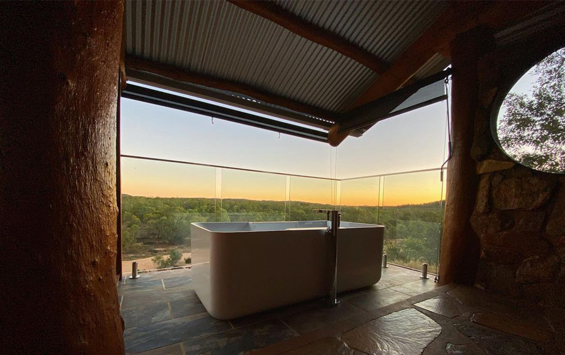 a white, freestanding bath sits on a balcony at sunset.