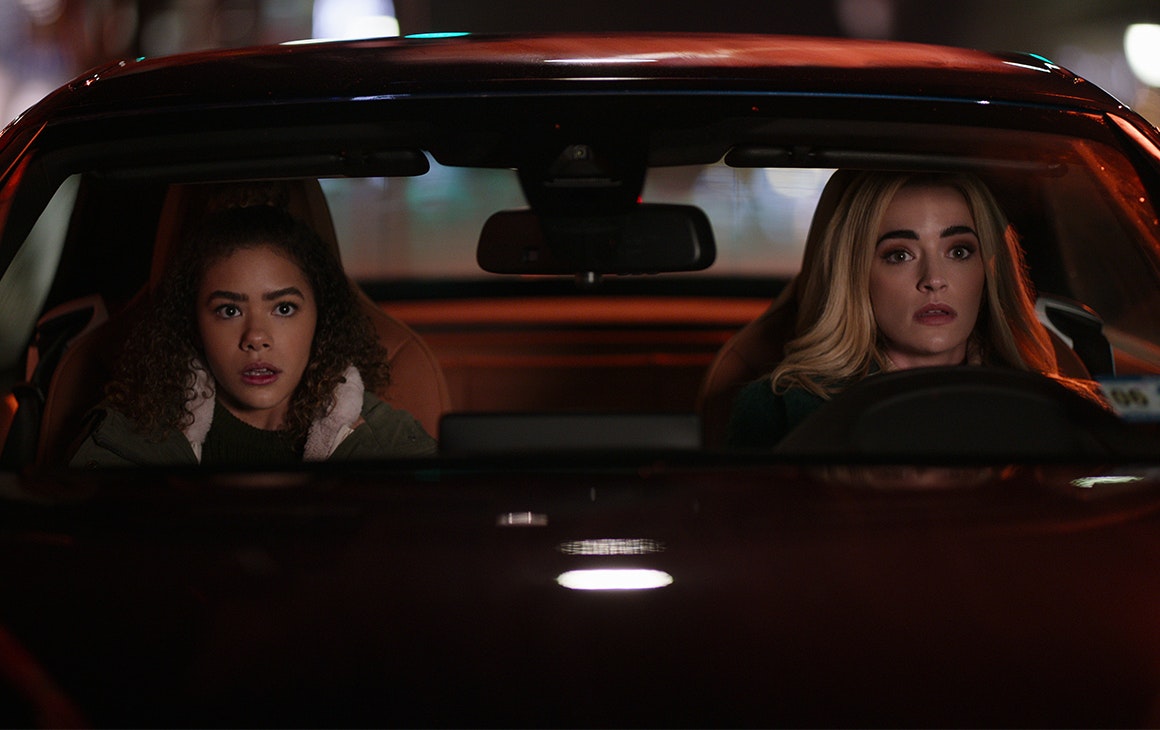 two young women sit behind the wheel of a parked car at night