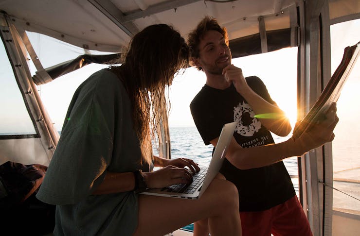 two people on a boat, one is on a laptop and the other is looking at a report