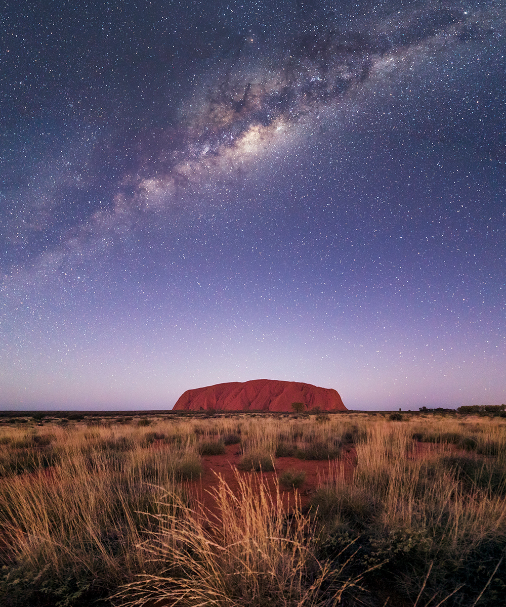 a sparkling night sky, full of stars, over the top of Uluru.