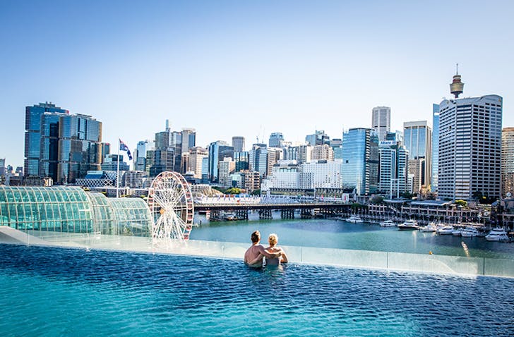 two people in infinity pool overlooking city