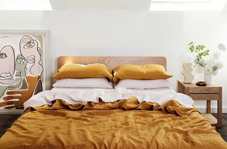 a double bed, with mustard coloured sheets and pillows. a framed piece of art sits next to the bed.