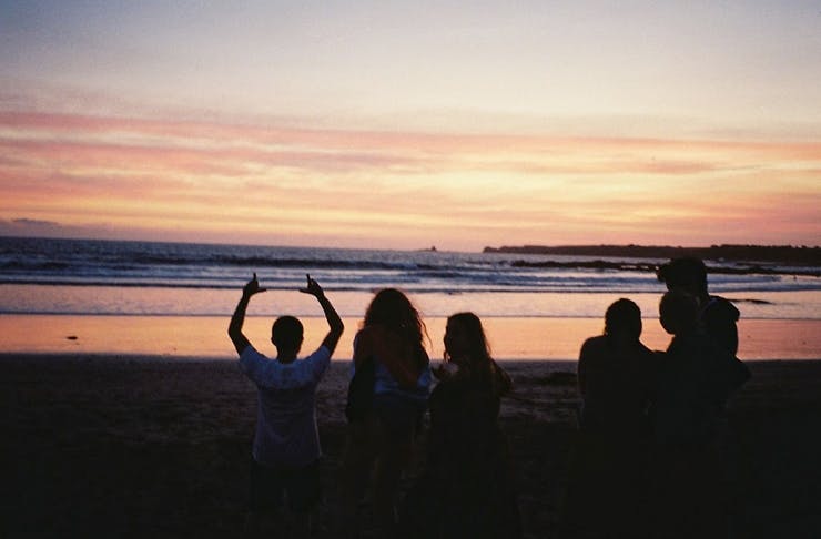 people standing on the beach at sunset