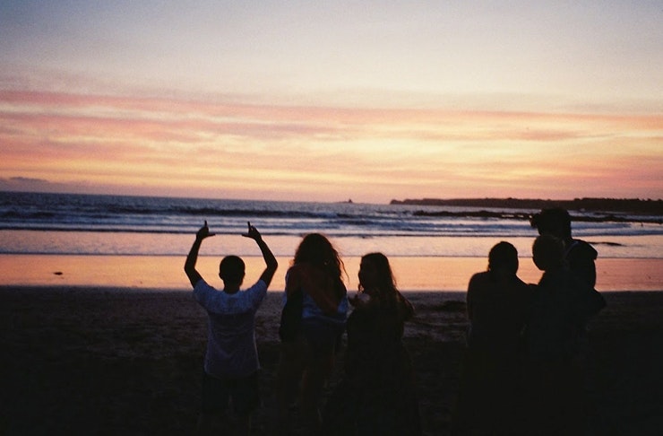 people standing on the beach at sunset