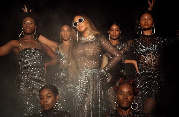 Beyonce on the set of Black Is King wearing big sunglasses and surrounded by a group of dancers.