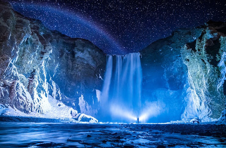 a person stands in front of the stunning Skógafoss, Iceland at night.