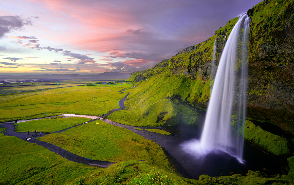 A stunning waterfall cascade down a bright green hill, with a dusty pink sunset in the background.