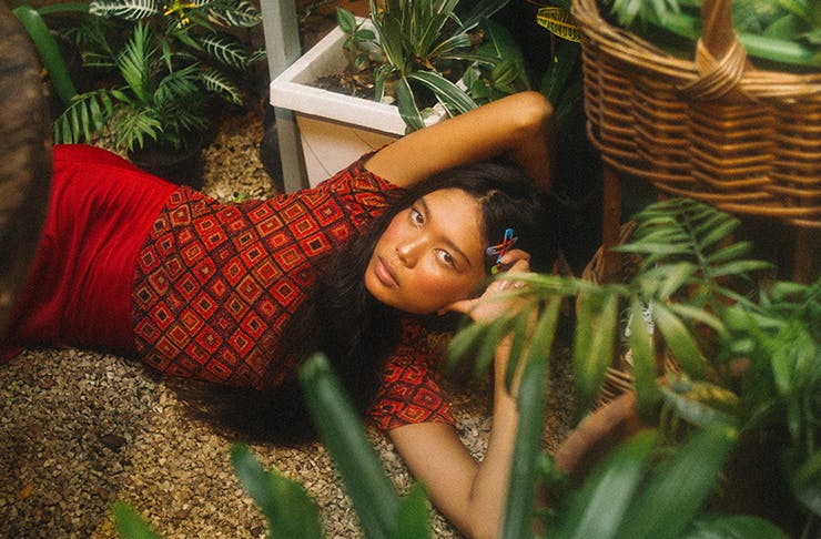 Woman laying on the ground in a red top among loads of indoor plants.