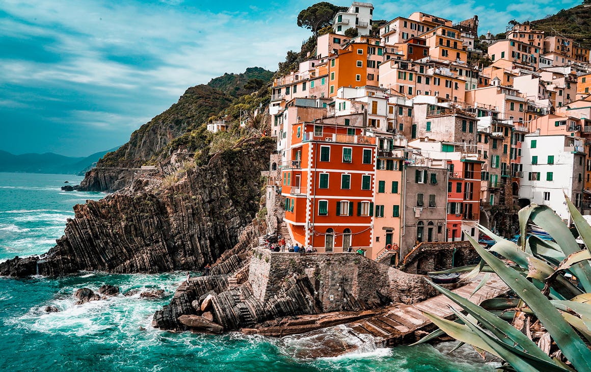 clusters of colourful building perch on the edge of a rugged coastline in Italy.