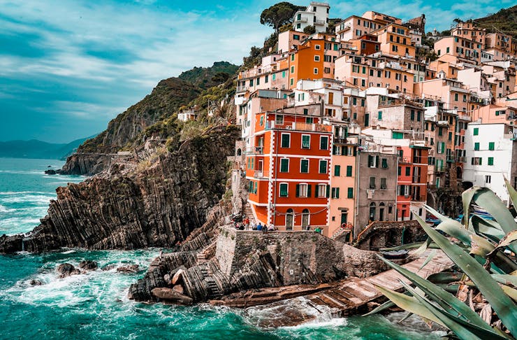 clusters of colourful building perch on the edge of a rugged coastline in Italy.