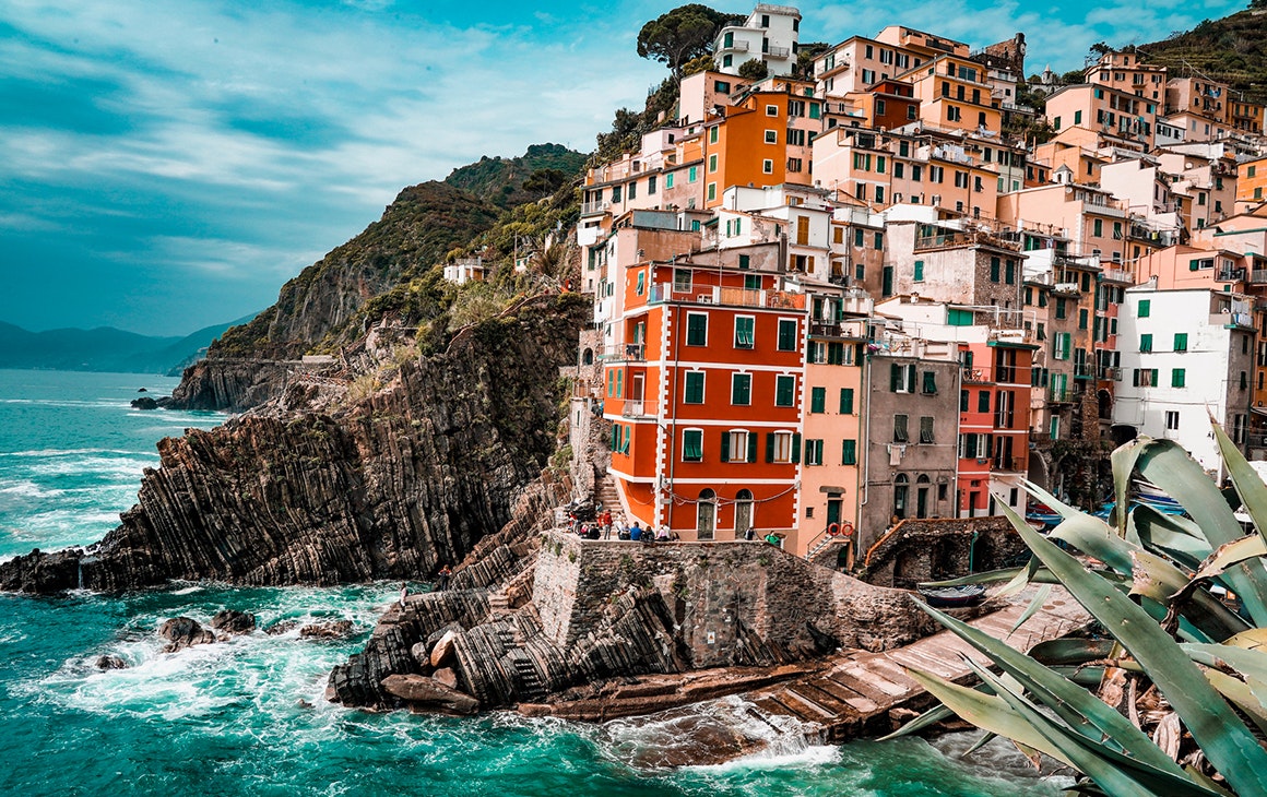 clusters of colourful building perch on the edge of a rugged coastline in Italy.