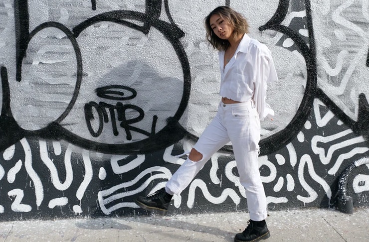 girl in ripped jeans and shirt standing in front of graffiti wall
