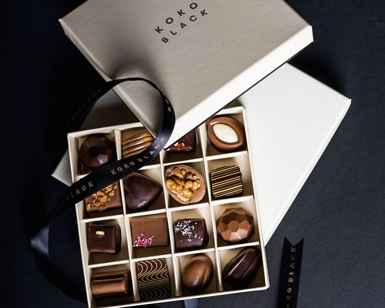 a white box lies open on a table, filled with various chocolate.