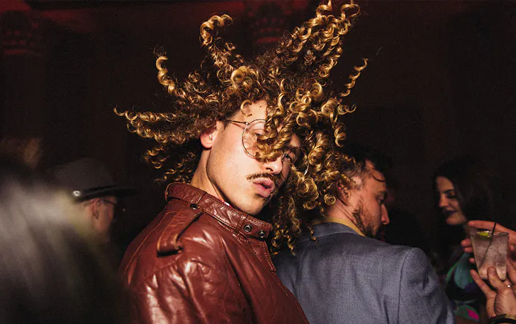 a man in a leather jacket flicks this hair in the air