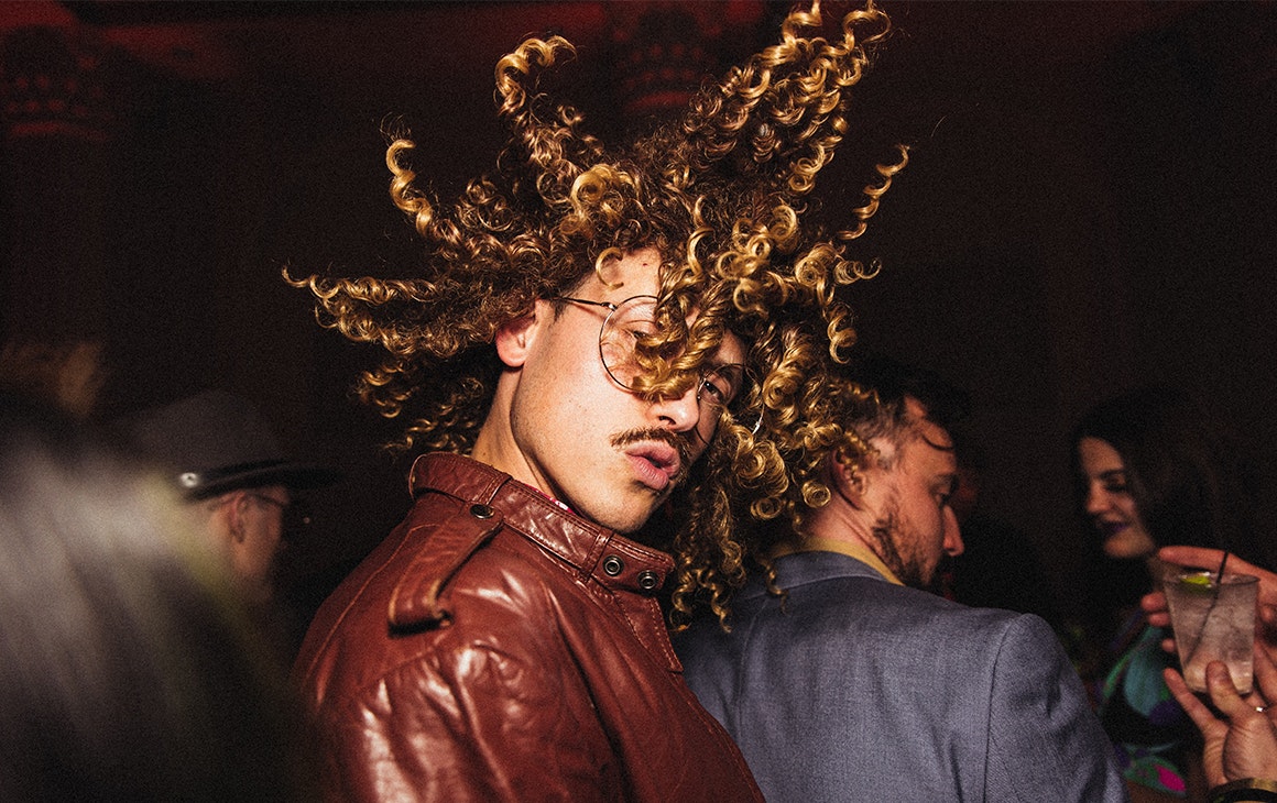 a man in a leather jacket flicks this hair in the air