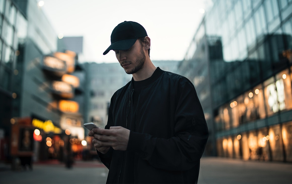 a man wearing a cap in the city plays on his phone.