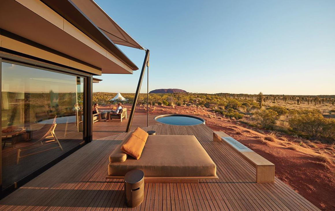 The exterior of a glamping tent featuring a dip pool, day bed and Uluru in the distance.