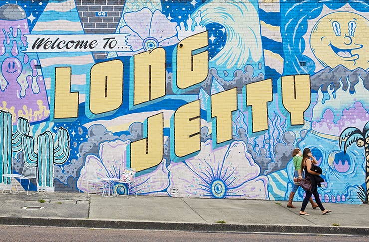 Colourful Long Jetty Mural along a brick wall with two women walking by.