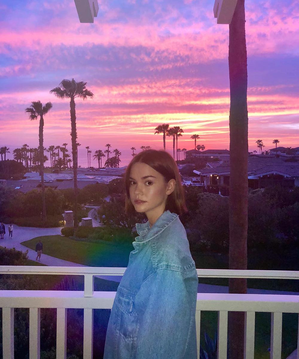 maia mitchell poses on a balcony with a stunning LA sunset behind filled with dreamy pink and dusty blues.