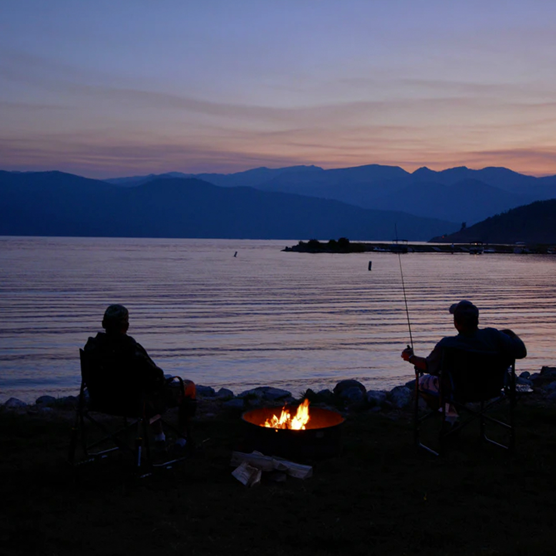 silhouette of people camping lakeside with campfire while fishing at night