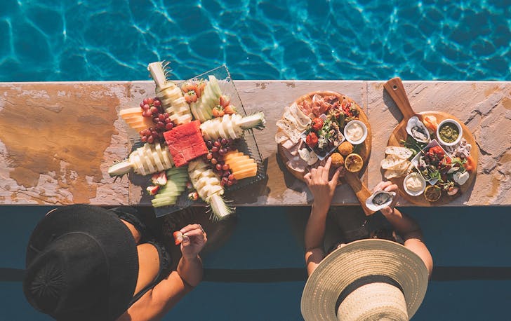 two women eat breakfast at the edge of a pool