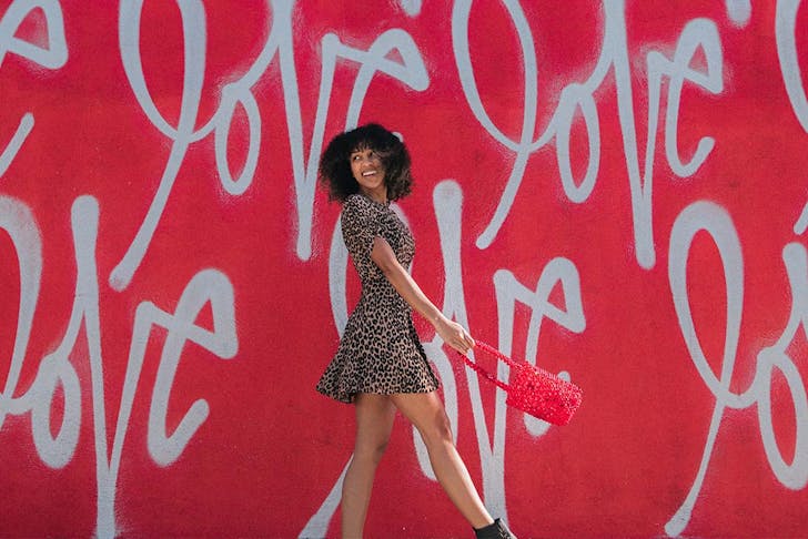 A woman smiles as she walks in front of a red wall with the word 'love' written all over it. 