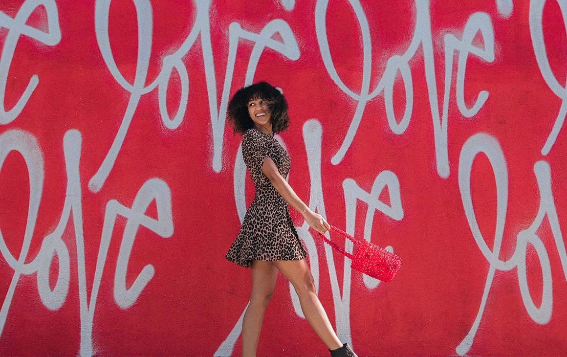 A woman smiles as she walks in front of a red wall with the word 'love' written all over it. 
