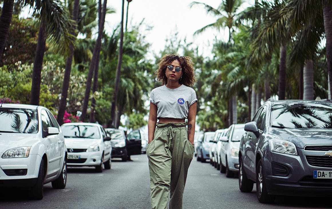 a woman, hands in her pockets, walks down a tree-lined street