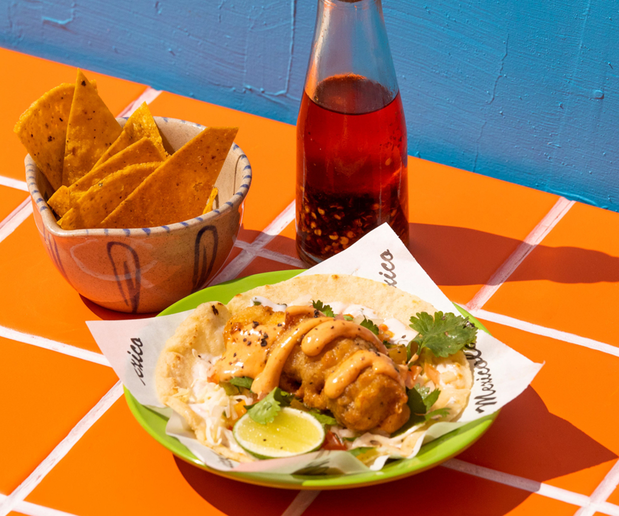 tacos and chips on tiled table with sangrita bottle