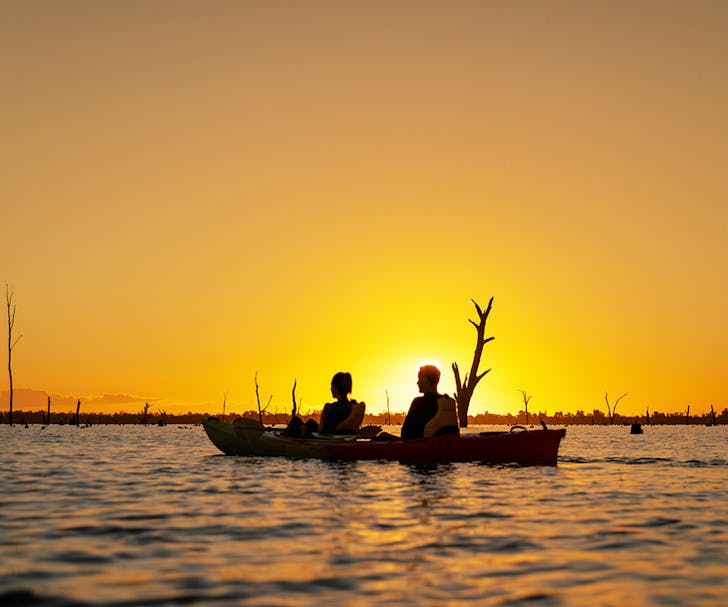 two people kayaking on river at sunset