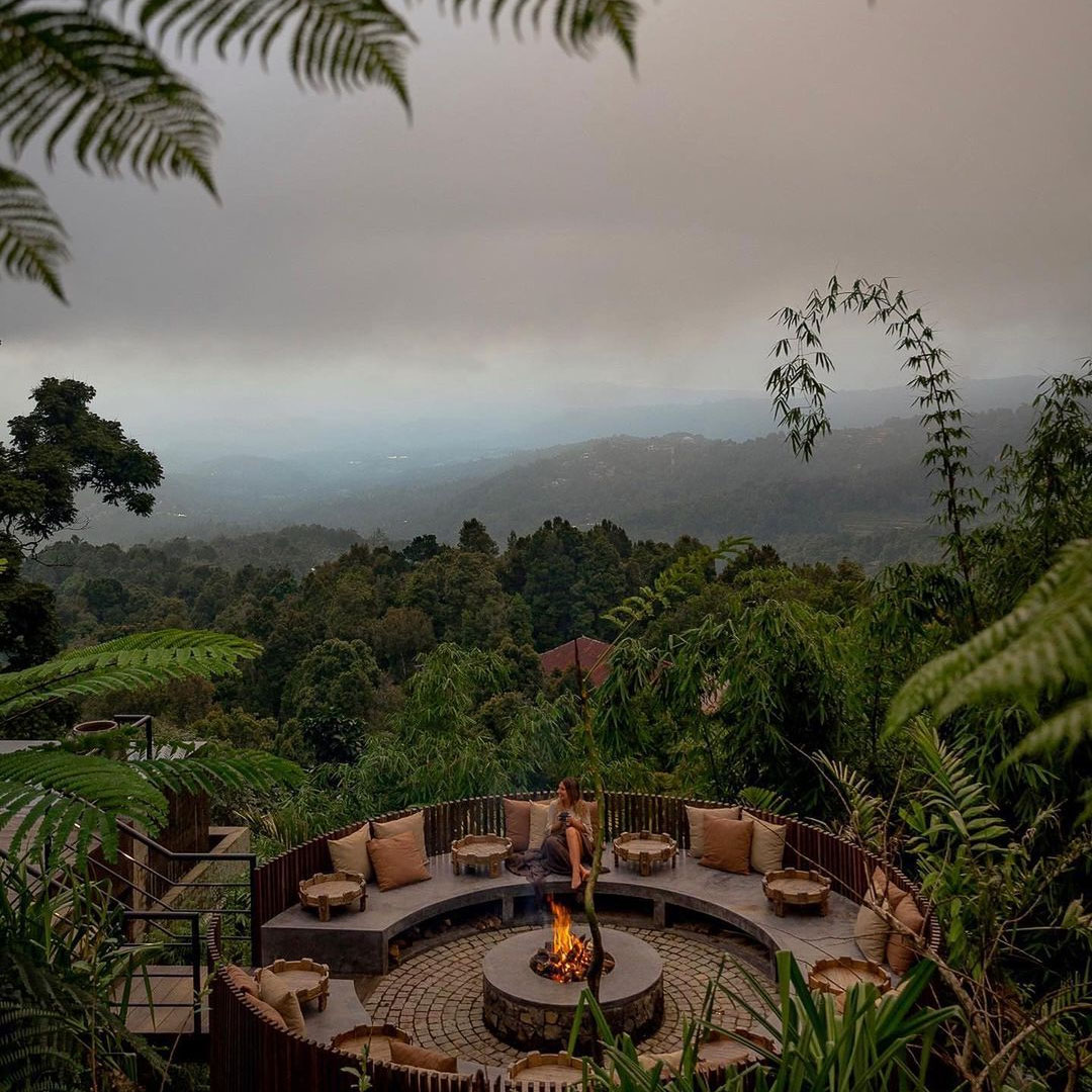 a person sitting at a firepit overlooking a jungle