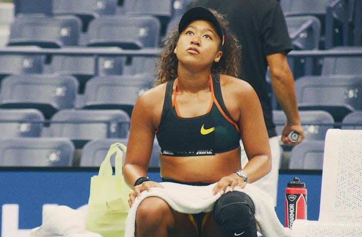 Naomi Osaka sits on the side of a tennis court