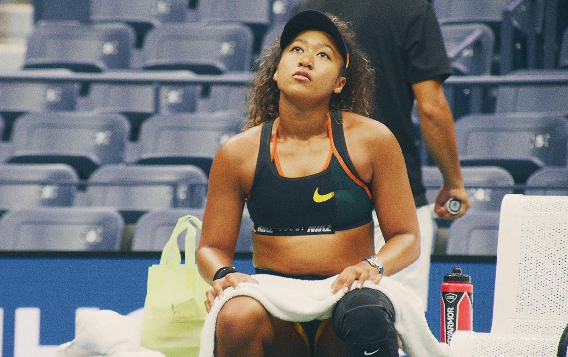 Naomi Osaka sits on the side of a tennis court