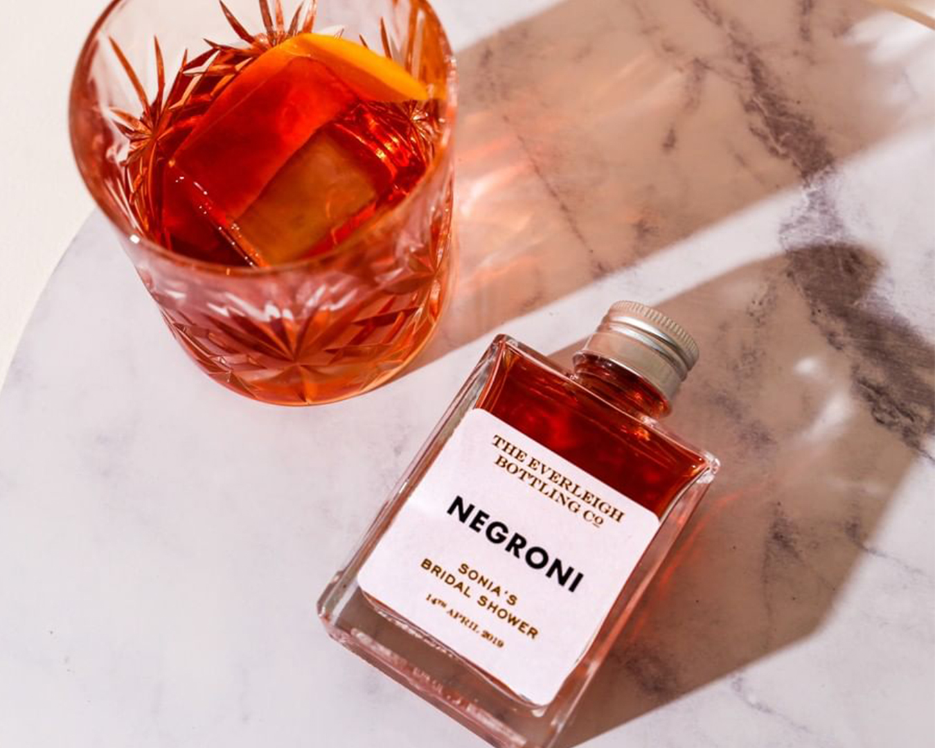 A glass and small bottle of negroni lay on a marble table.