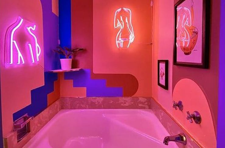 Bathroom with neon pick lighting and neon art of women's bodies on the wall.