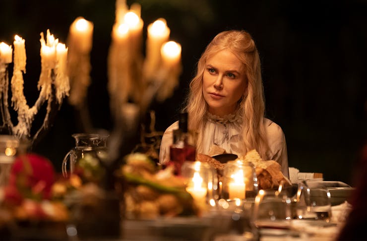 Nicole Kidman in Nine Perfect Strangers sits at a dinner table laden with candles and food.