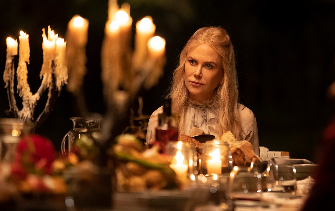 Nicole Kidman in Nine Perfect Strangers sits at a dinner table laden with candles and food.
