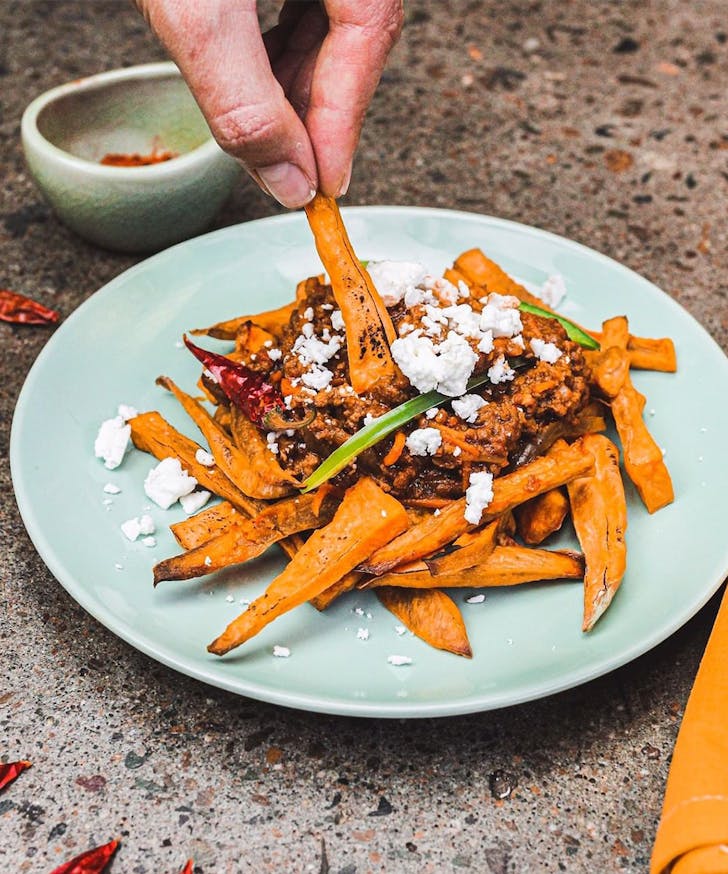 a plate of sweet potato fries with a finger picking at them