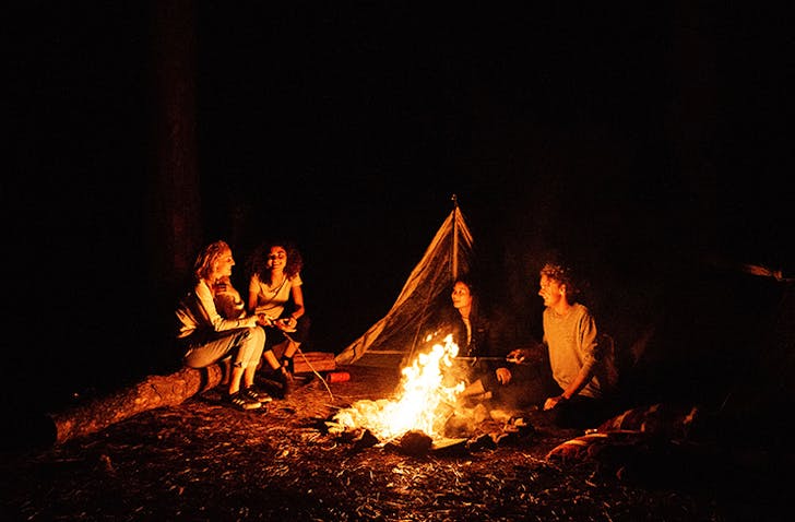 people sitting around a campfire in a forest at night