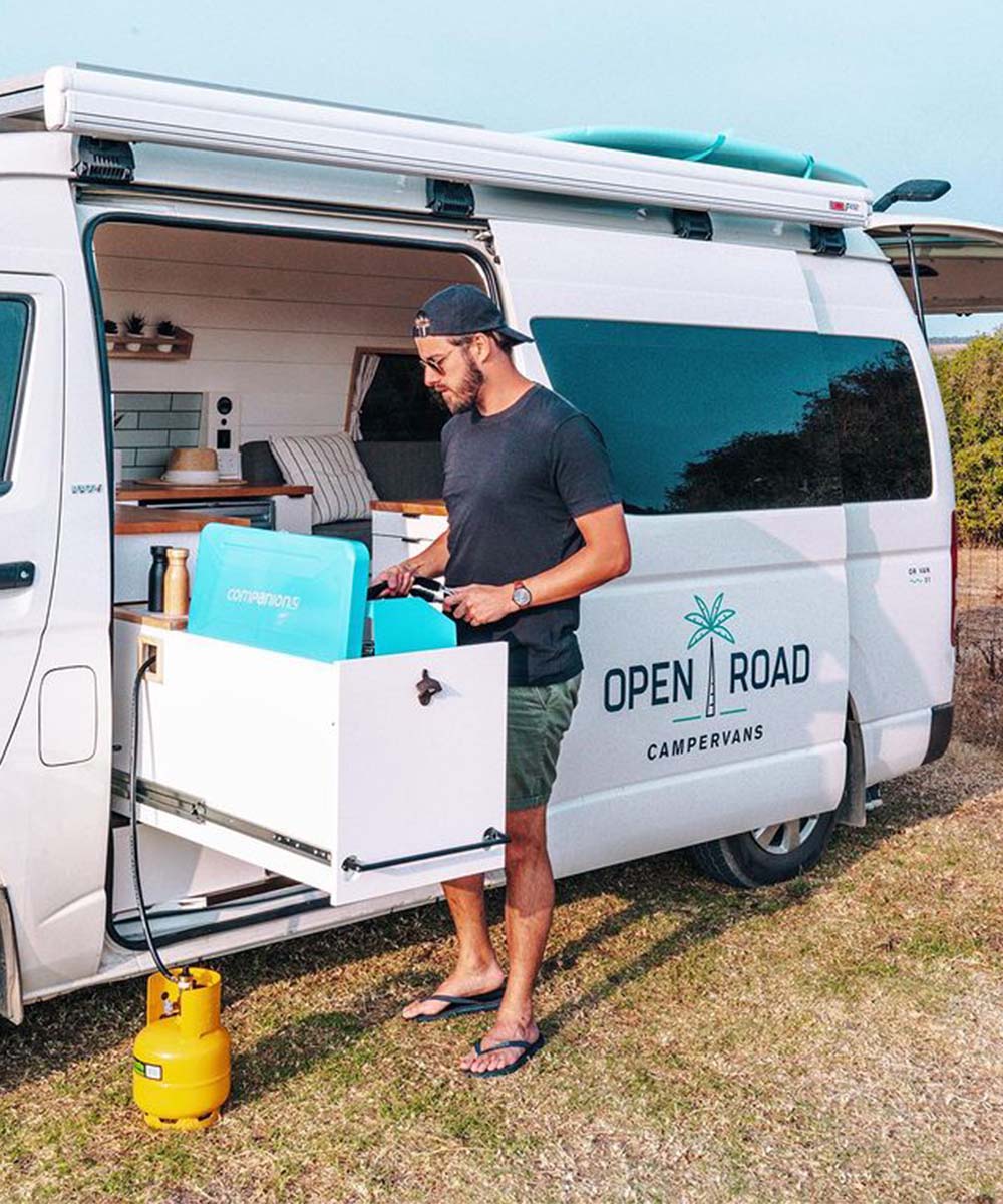 A man cooks next to the Open Road Campervan