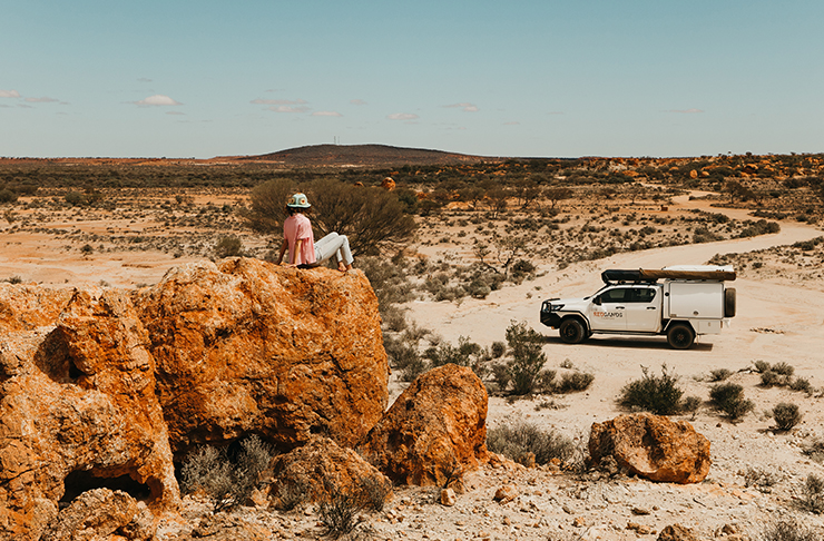 person sitting on cliff lookout out in desert