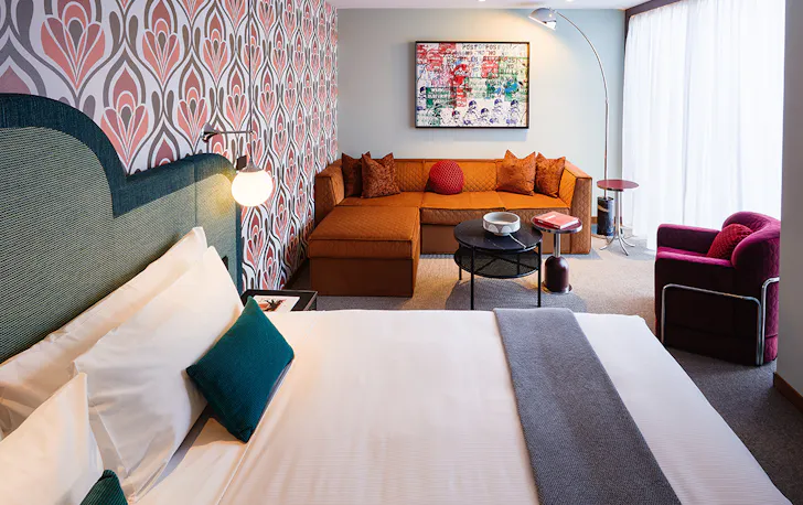 A plush king bed sits against a pink patterned wallpaper inside a suite at the Ovolo South Yarra